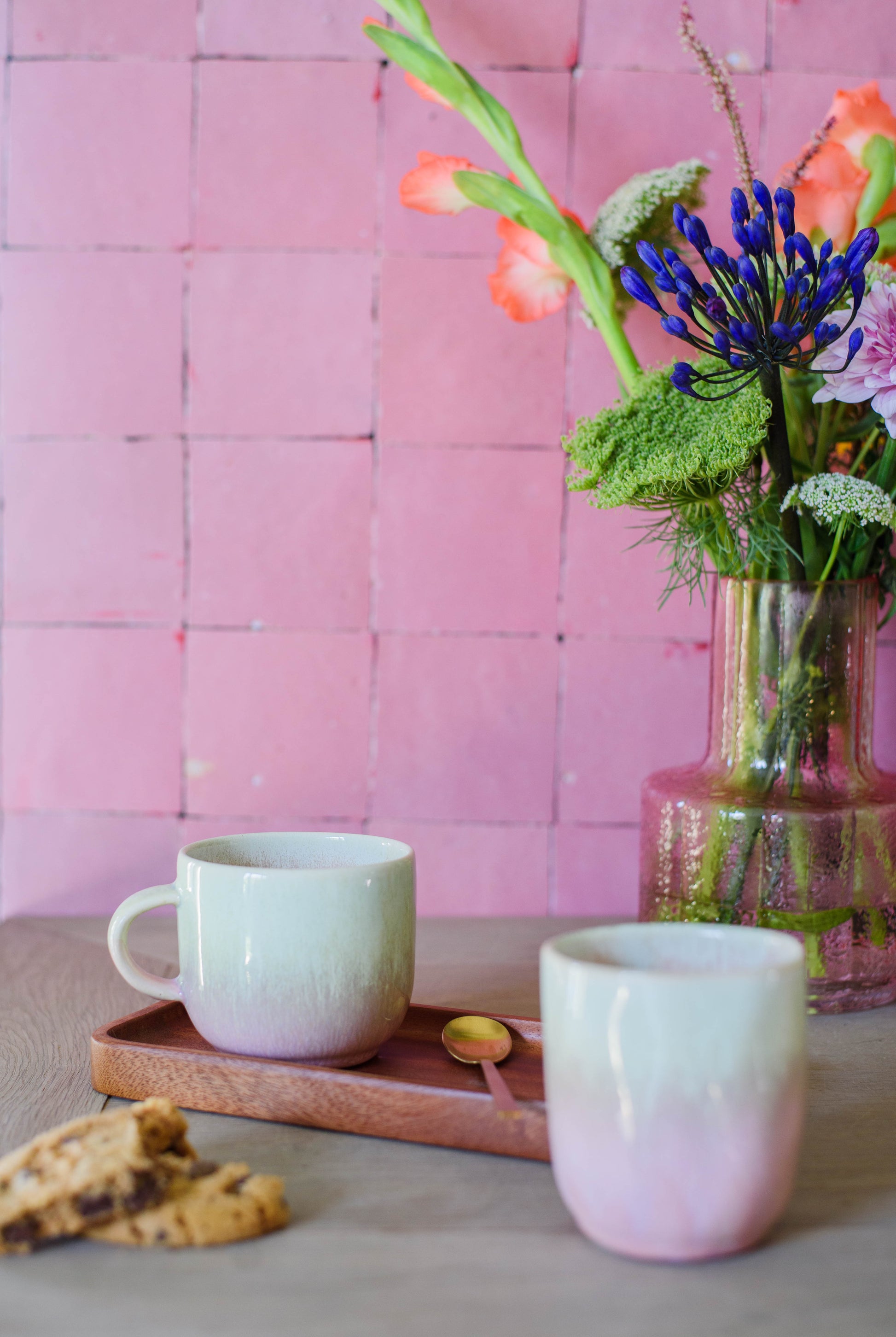 2 handgemaakte keramieken mokjes op tafel in dezelfde kleurstelling groen en roze, eentje met oor en eentje zonder oor