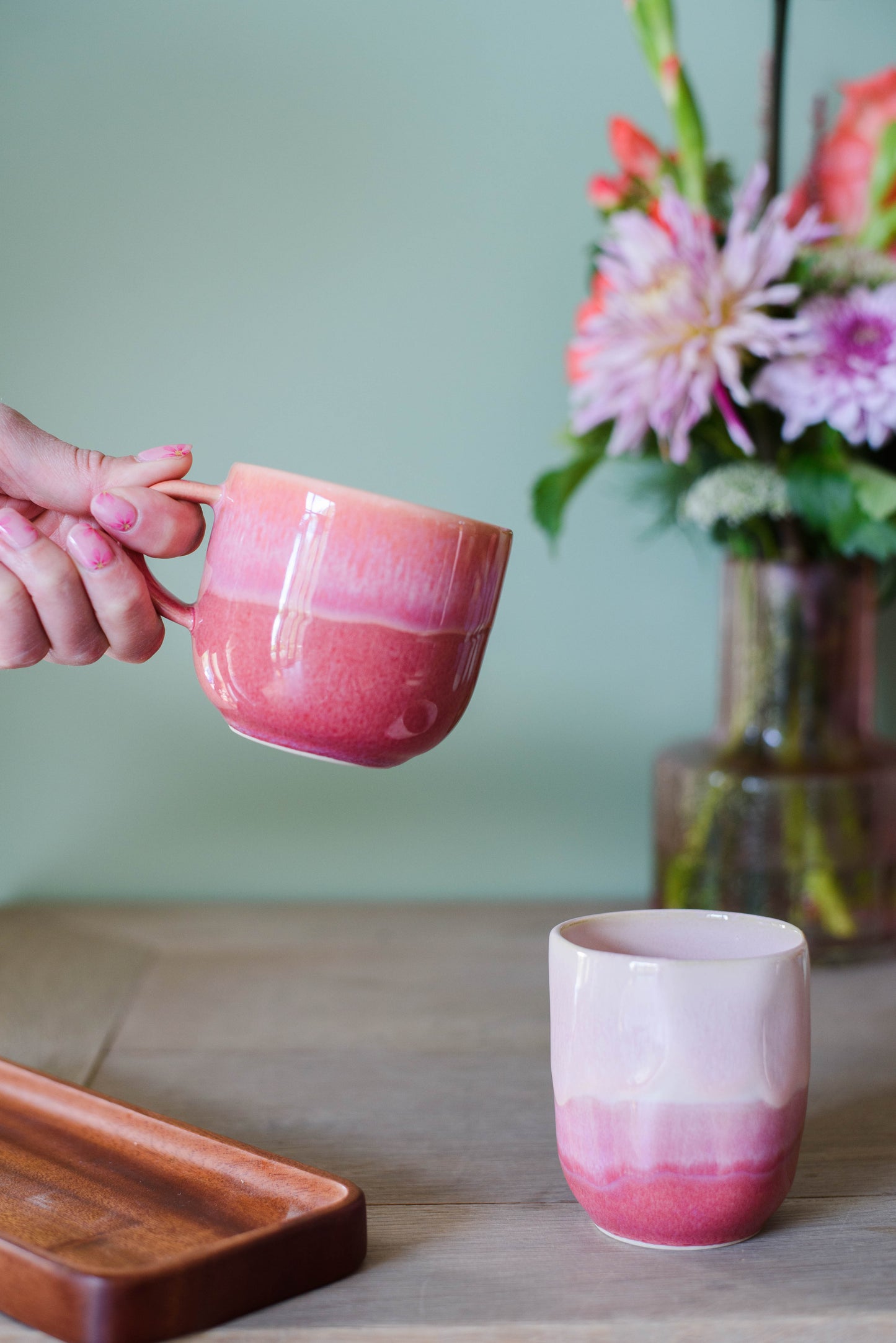 sfeerfoto met 2 koffiemokken in de kleuren roze en een hand die 1 kopje vasthoudt