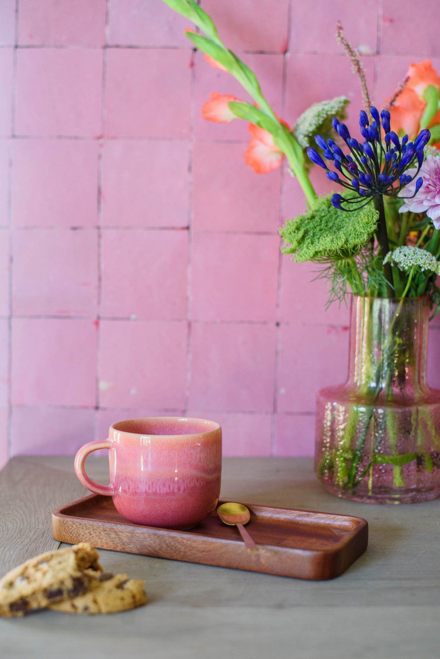 sfeerfoto van een roze wand, vaas bloemen en roze koffiemok van handgemaakt keramiek
