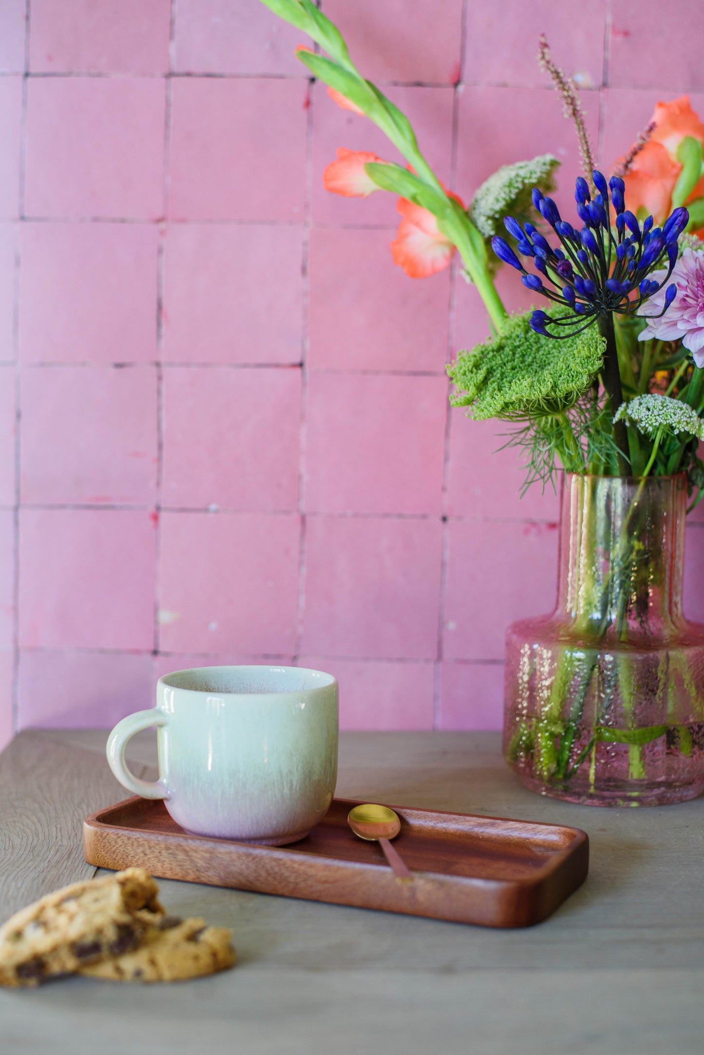 sfeerfoto van mok met oor in groen roze voor roze muur en op serveerplank met lepel